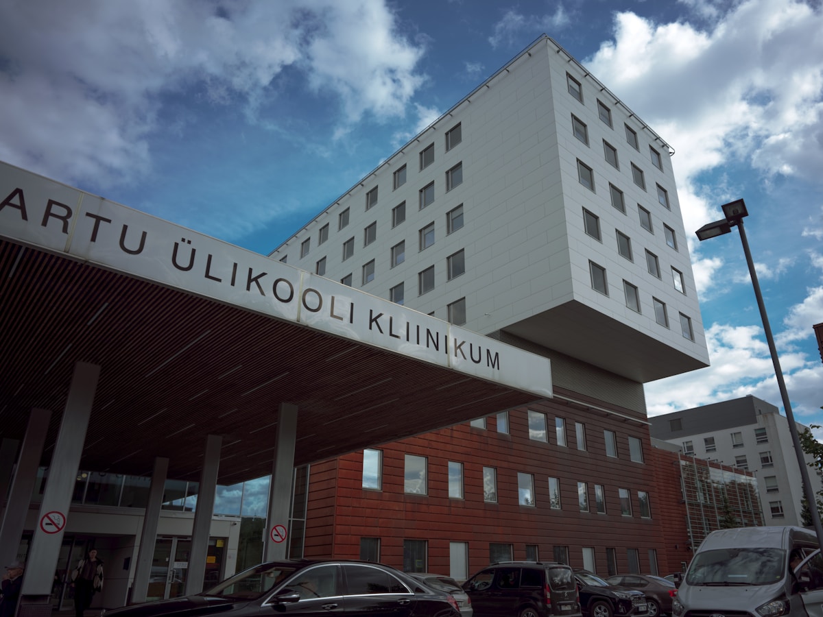 Modern hospital building with a sign reading TARTU ÜLIKOOLI KLIINIKUM under a cloudy sky